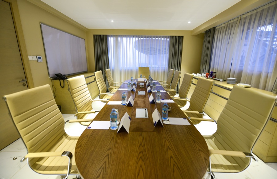 One of Skyz Hotel Kampala's boardrooms with an oval table, cream leather chairs and sheer curtains