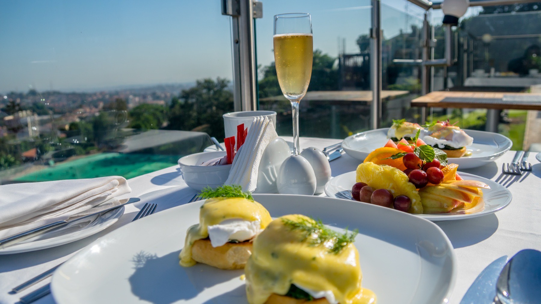 A breakfast tray with eggs benedict and a city view, served in-room at Skyz Hotel Kampala