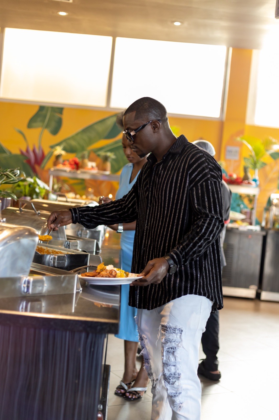 A guest serving himself at the buffet against the tropical mural at The Kampala Style Brunch, December 2024