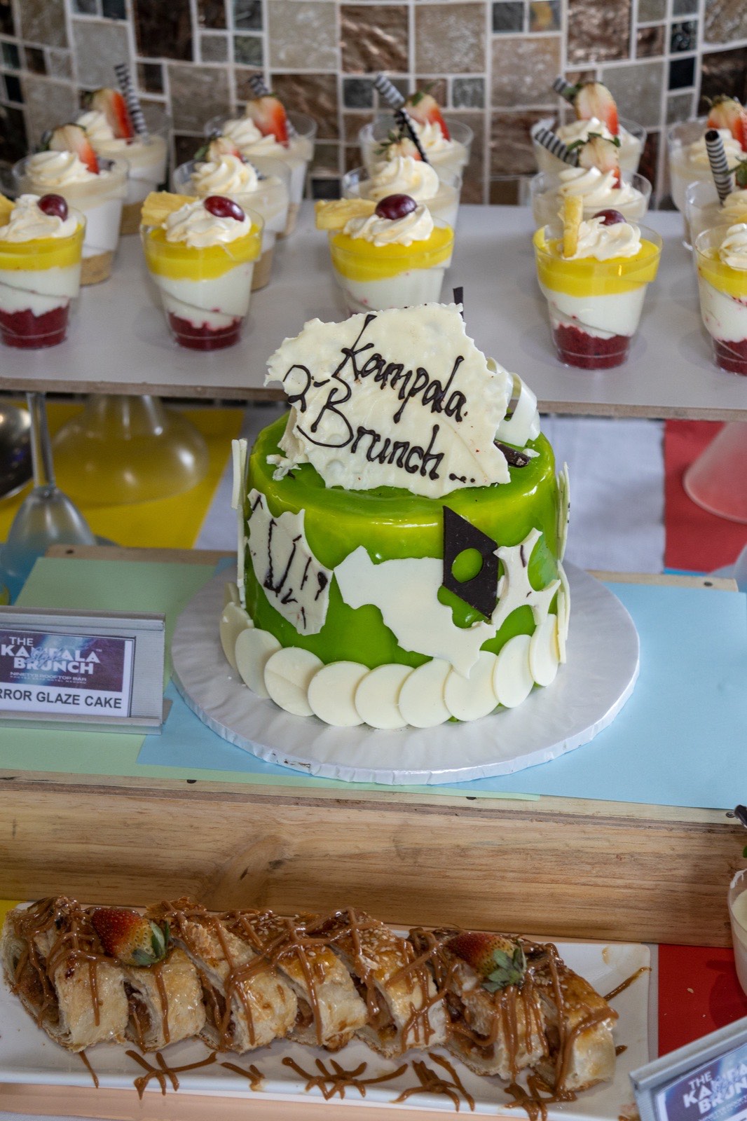 A green mirror-glaze cake branded for The Kampala Brunch on the dessert table, September 2024