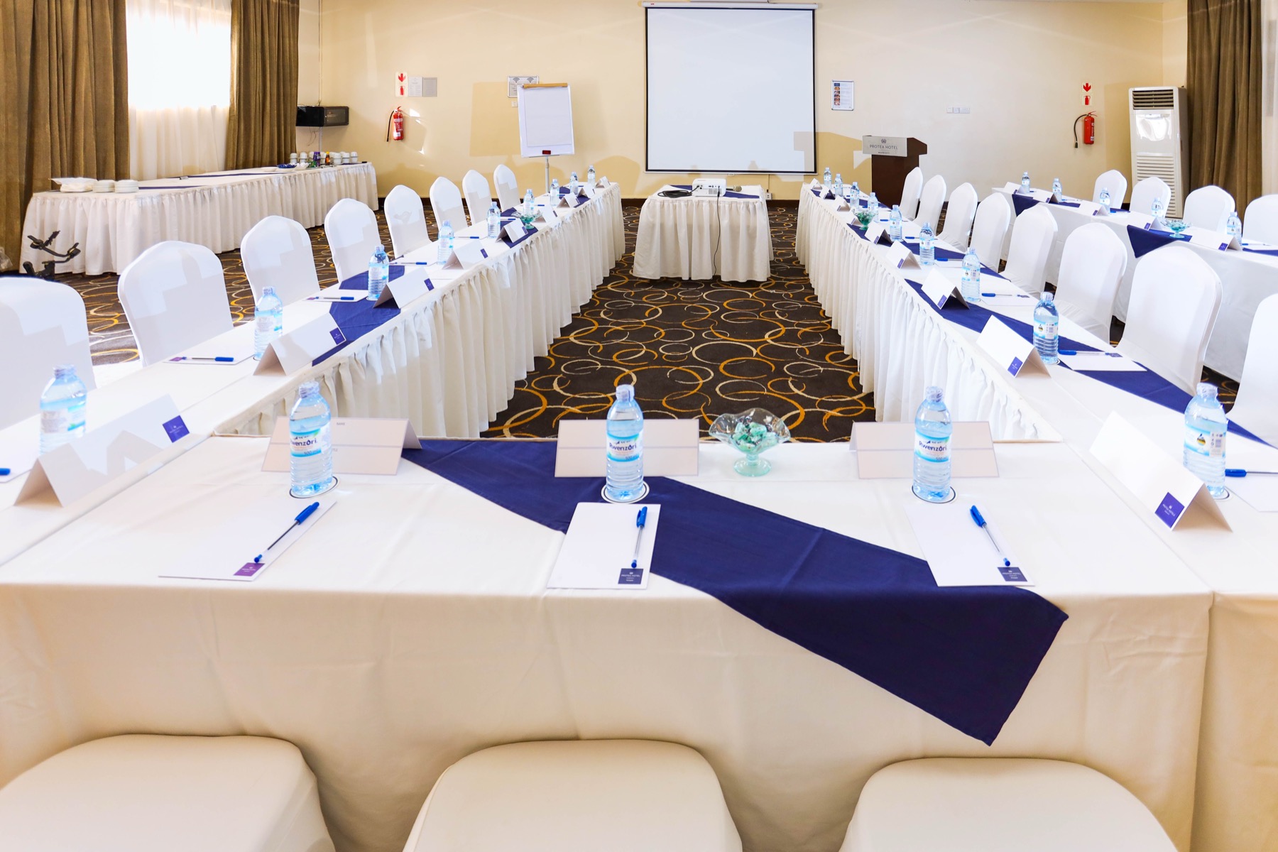 A Skyz Hotel Kampala meeting room facing a projector screen with a flip chart