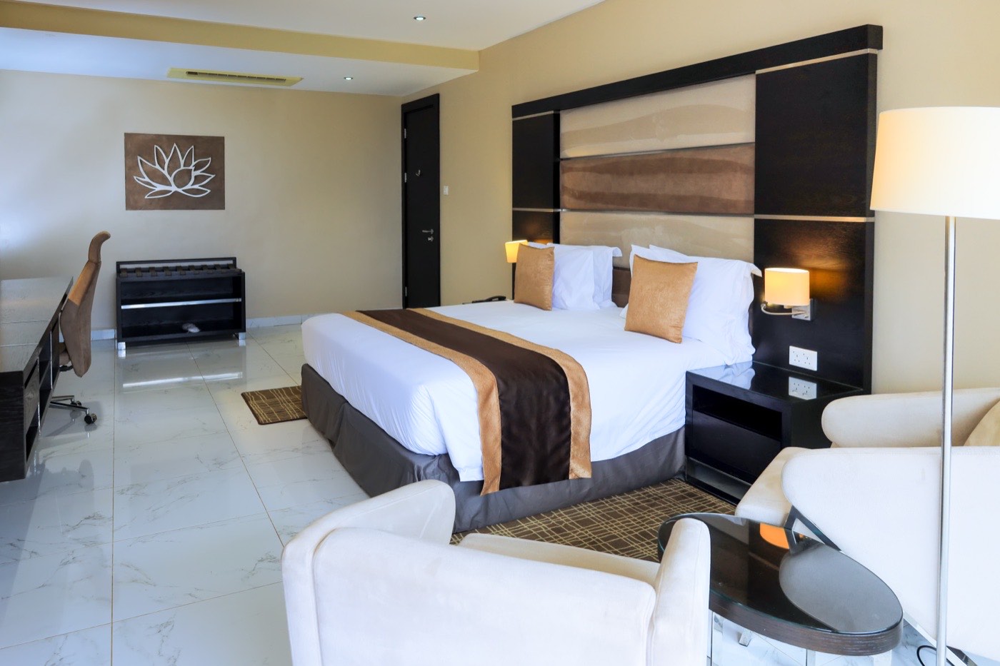 Standard Room bedroom at Skyz Hotel Kampala with a plush bed, padded tan and brown headboard, lotus-flower wall art and a work desk